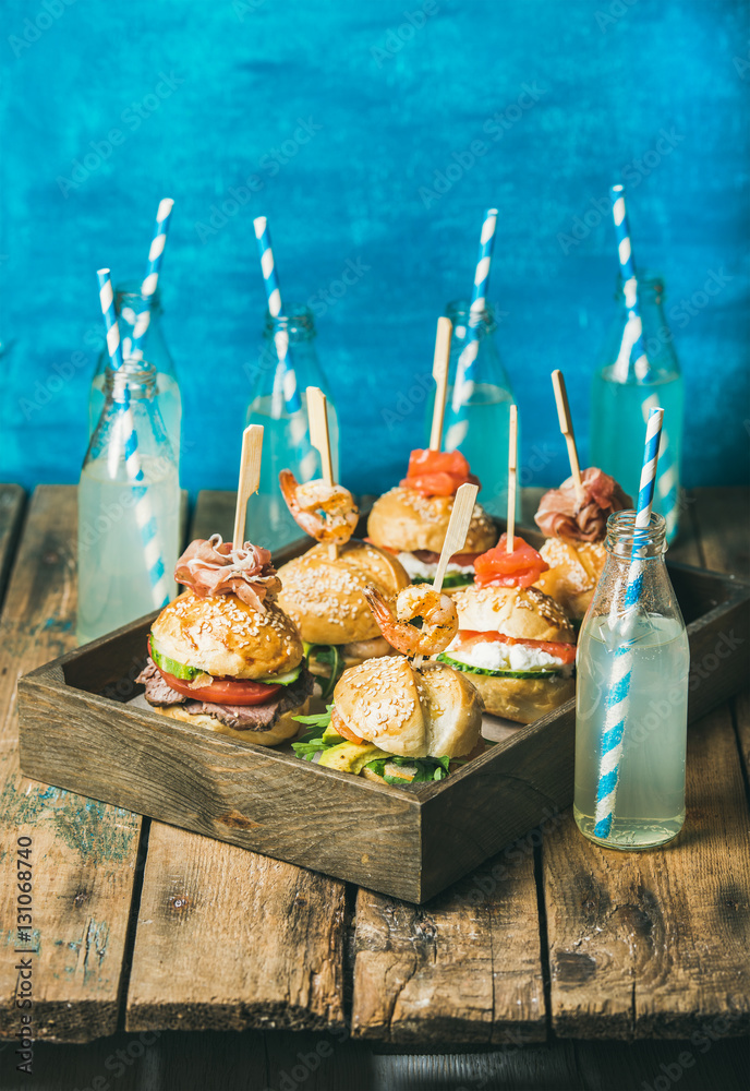 Home party food concept. Different burgers with sticks in wooden tray and lemonade in bottles with s