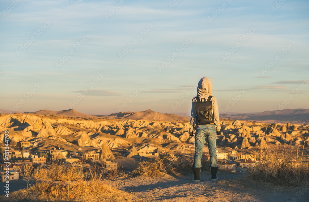 Young woman traveller wearing hoodie, backpack and jeans standing backwards and watching sunrise in 