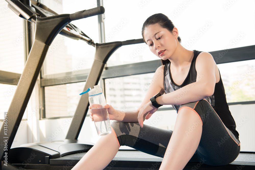 运动女性在跑步机上休息使用智能手表饮用水