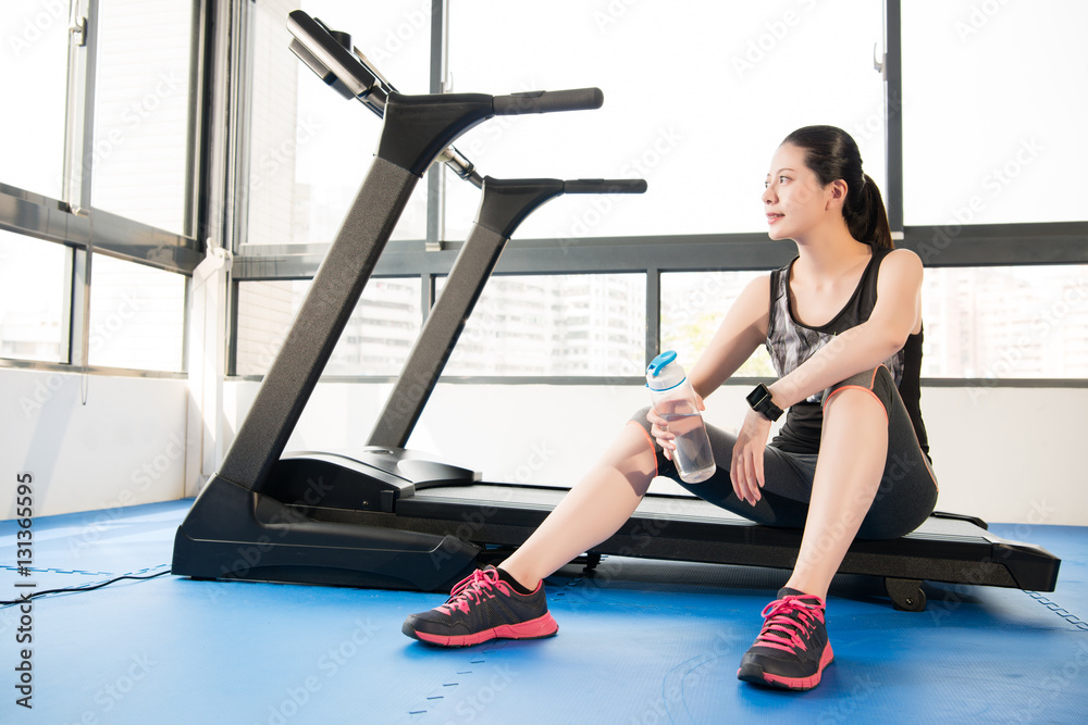 运动女性在跑步机上休息，使用智能手表喝水