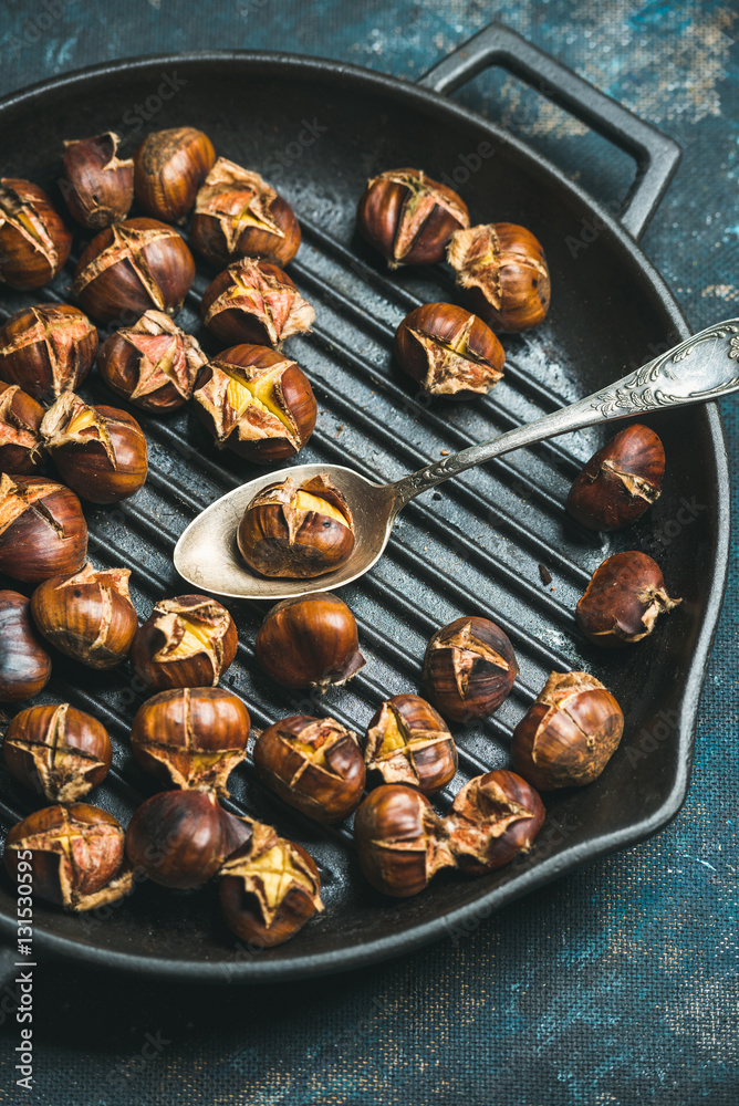 Close-up of roasted chestnuts and spoon in cast iron grilling pan over dark blue shabby plywood back