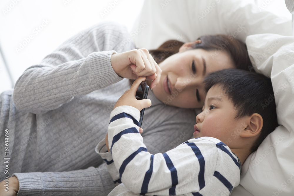 Mother and child lie down in bed and watch smartphone together