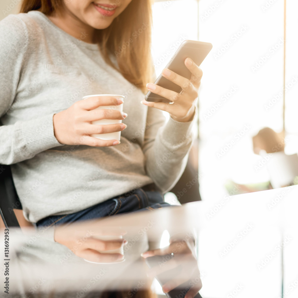 Woman using smartphone in coffee shop with image reflection on g