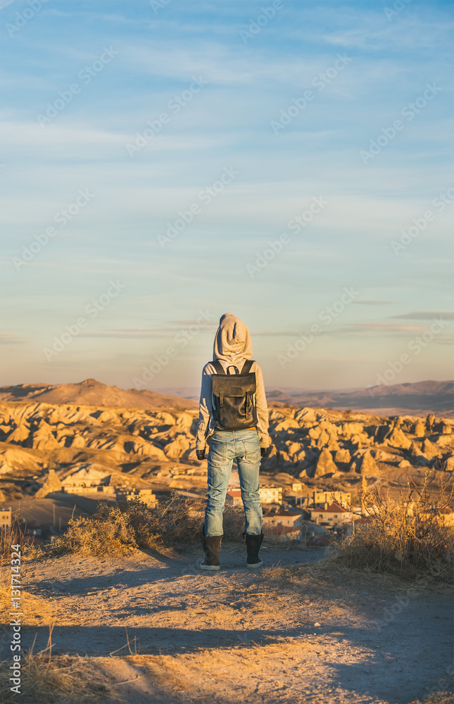 穿着连帽衫、背包和牛仔裤的年轻女性旅行者站在山上看日出