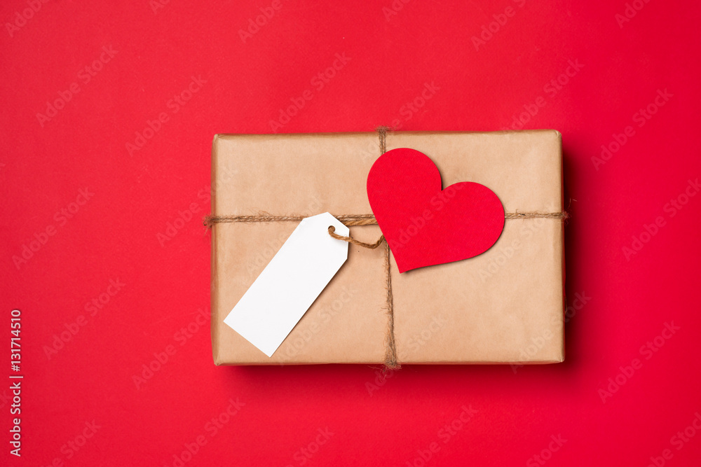 Handmade small gift box with heart symbol on red background.