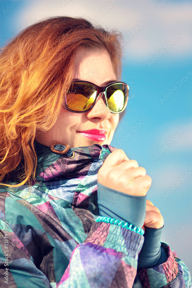 girl in a ski jacket and stylish glasses against the sky