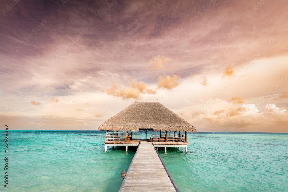 Wooden jetty leading to relaxation lodge. Maldives islands at sunrise