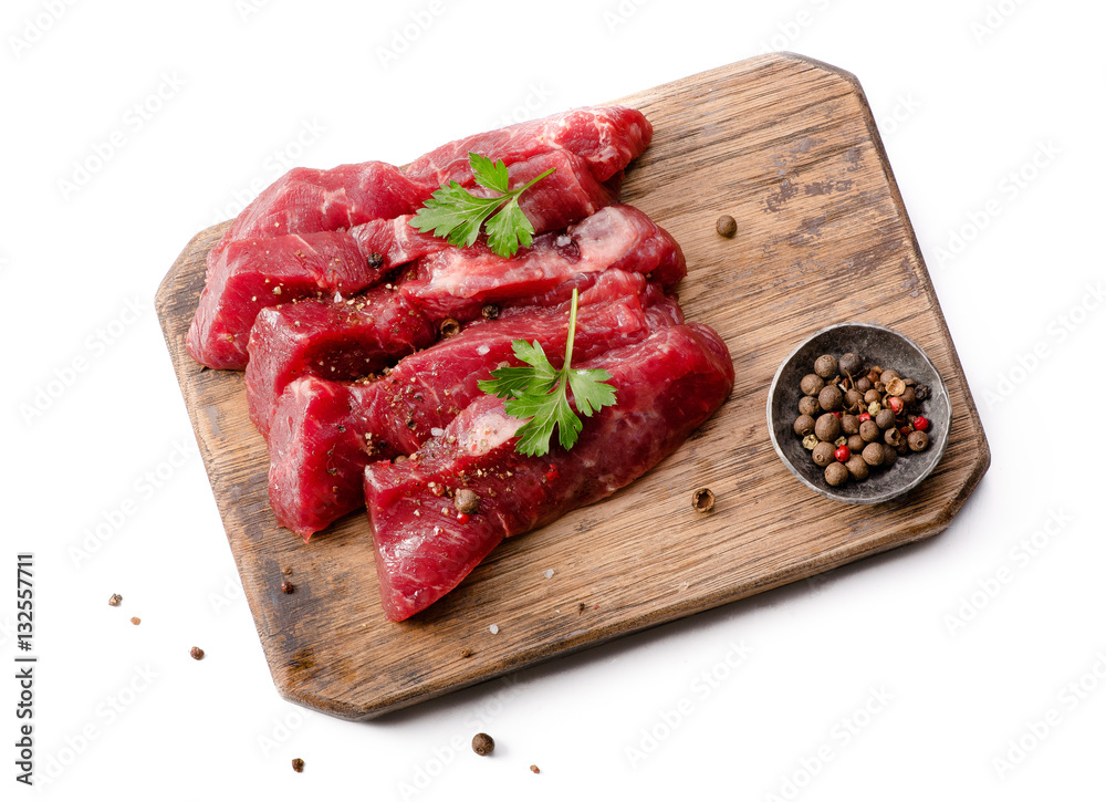 Pieces of meat with herbs, parsley and spices on wooden board isolated. Raw beef.