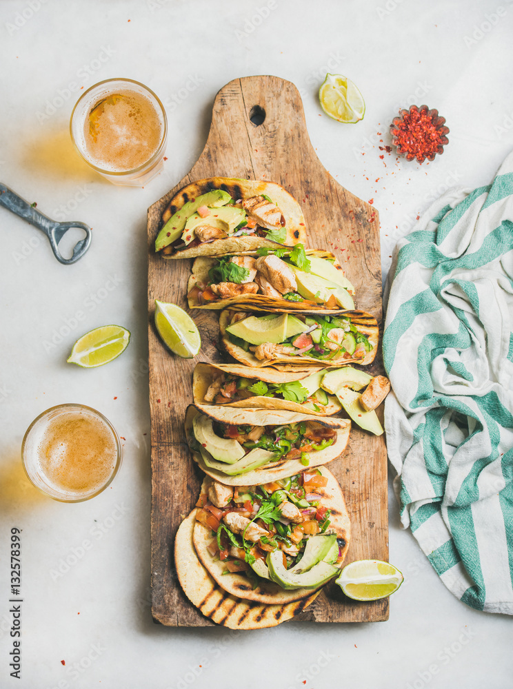Healthy corn tortillas with grilled chicken, avocado, fresh salsa, limes on wooden board and beer in