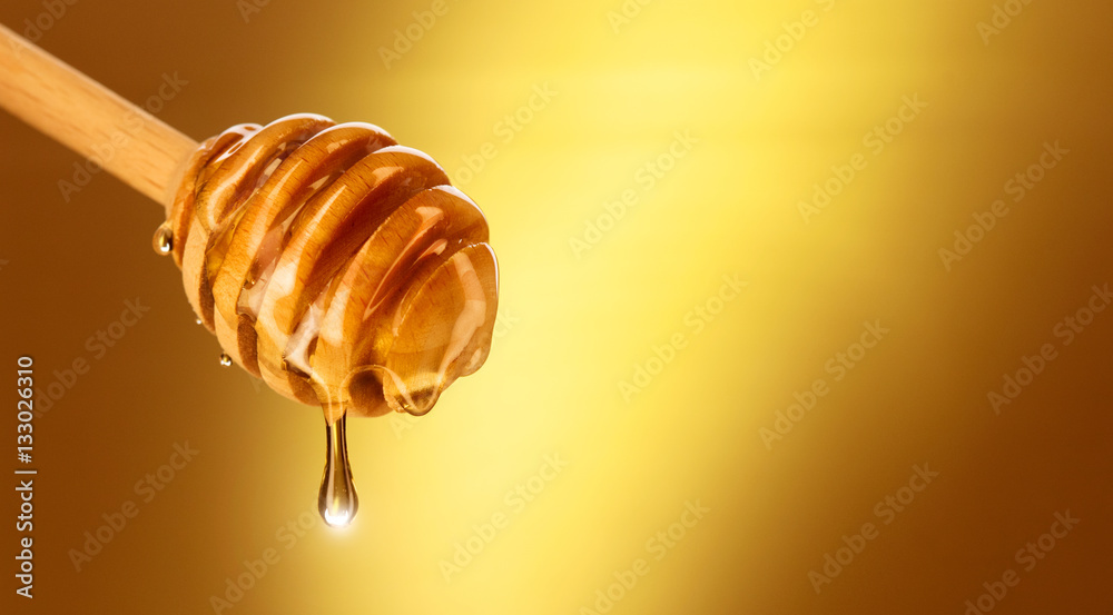 蜂蜜从黄色的蜂蜜勺中滴下。从木制蜂蜜勺中蘸下厚厚的蜂蜜