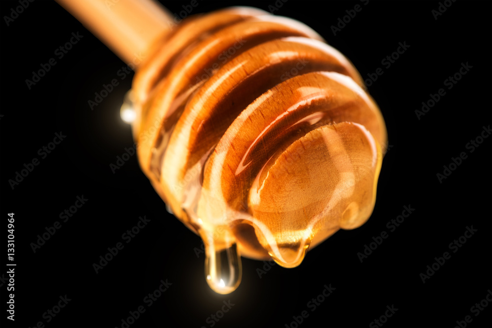 Honey dripping from honey dipper isolated on black. Thick honey dipping from the wooden honey spoon