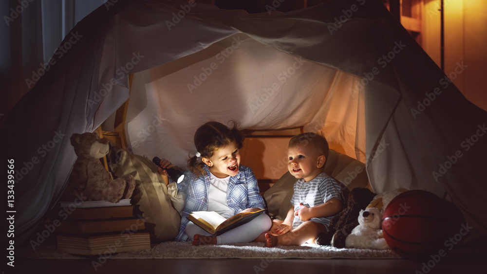 children boy and girl reading book with  flashlight in  tent