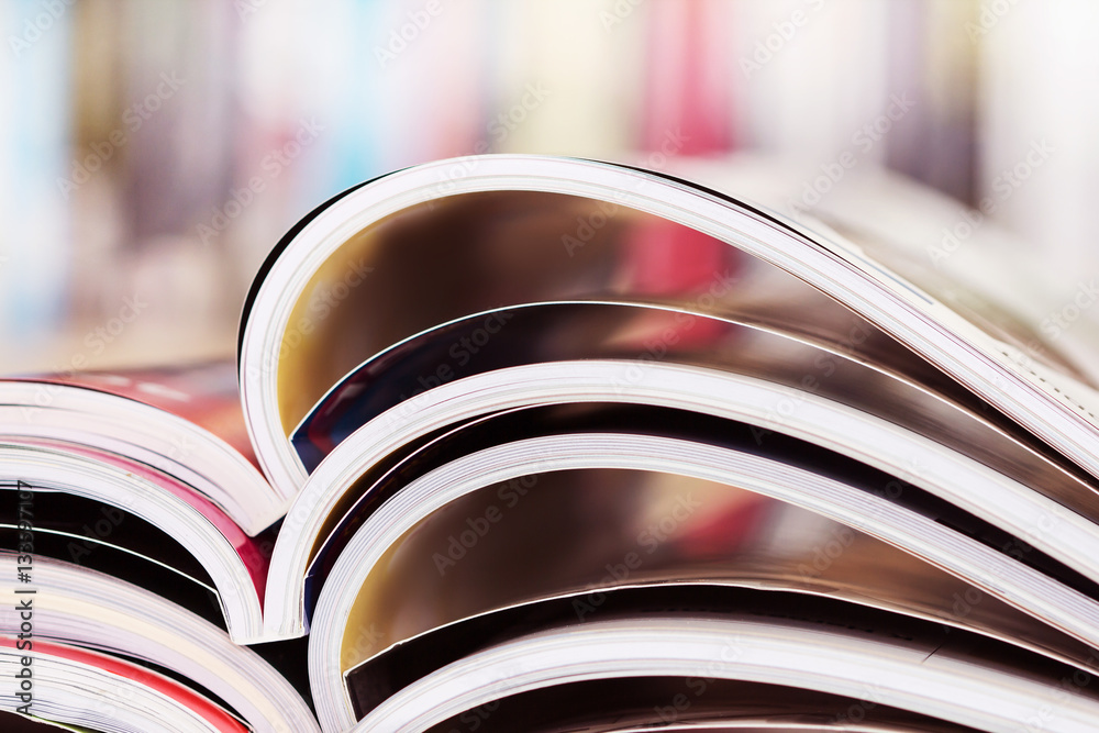close up stacking of opened magazine with blurry bookshelf 
