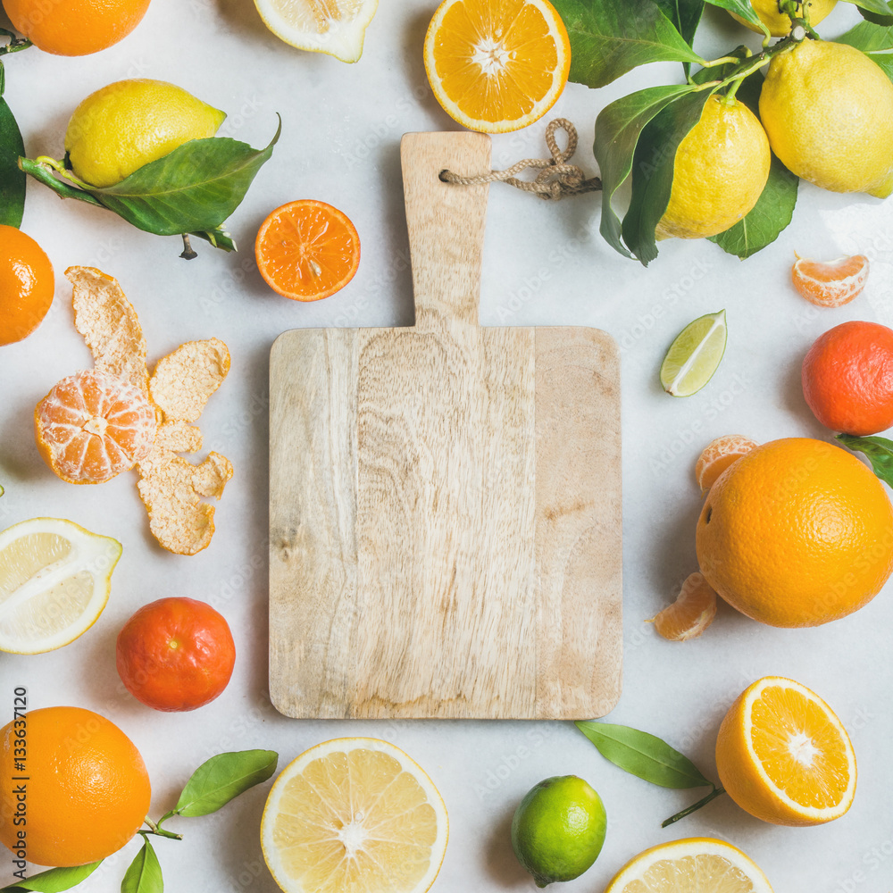 Variety of fresh citrus fruit for making juice or smoothie and wooden chopping board over light grey
