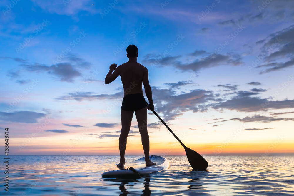 Silhouette of stand up paddle boarder paddling at sunset, sea