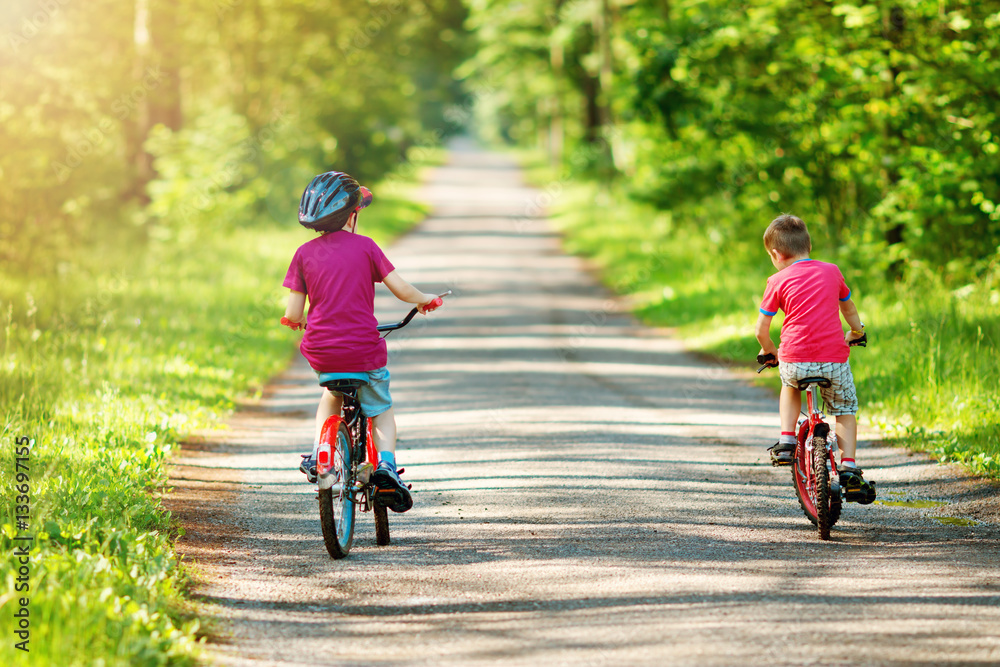 children riding on a bicycles at asphalt road in the park in summer