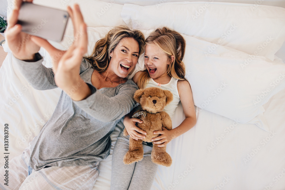 Young mother taking selfie with her daughter on bed