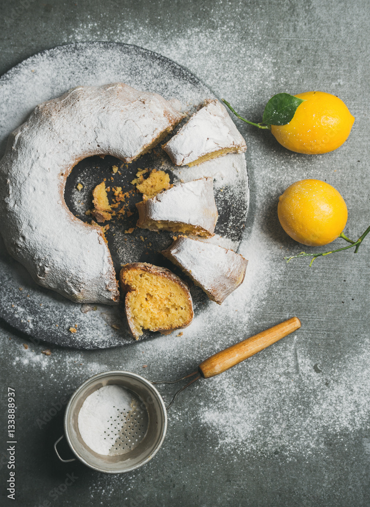 Homemade gluten-free lemon bundt cake with sugar powder served with freshly picked lemons over grey 
