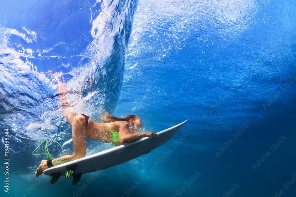 Active girl in bikini in action. Surfer woman with surf board dive underwater under breaking big wav