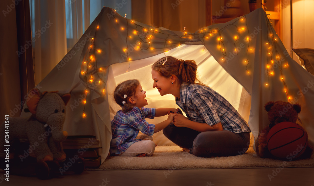 幸福的母亲和女儿在家里的帐篷里玩耍。
