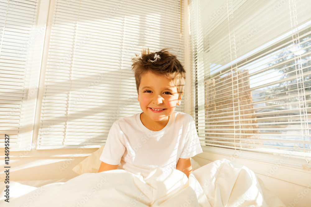 Cute boy awaking in white bedroom full of sunlight