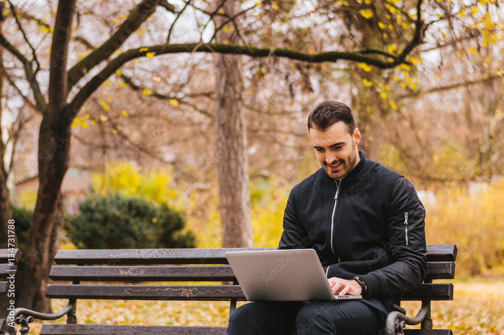 Young man sitting on the park bench with laptop