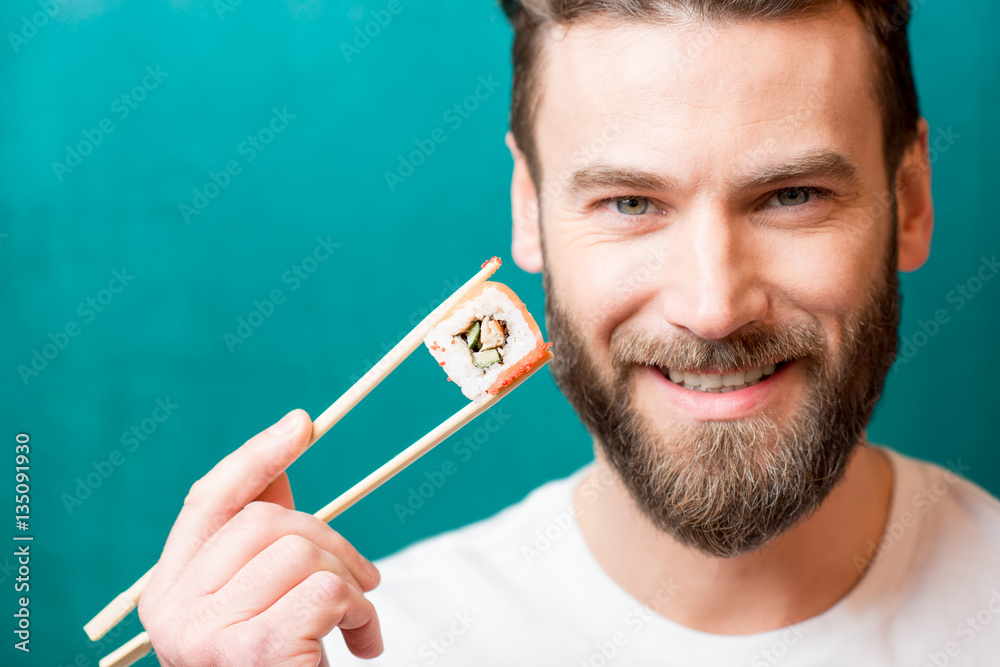 Close-up portrait of a man holding sushi with chopsticks on the green background
