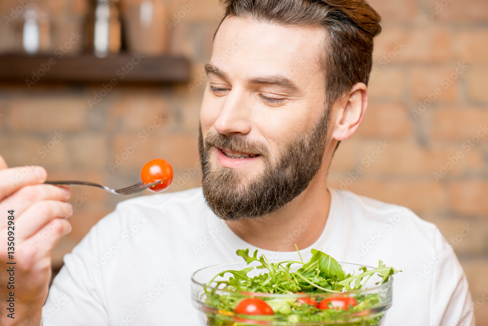Close-up portrait of a man eating salad with tomatoes on the red brick wall background. Healthy and 