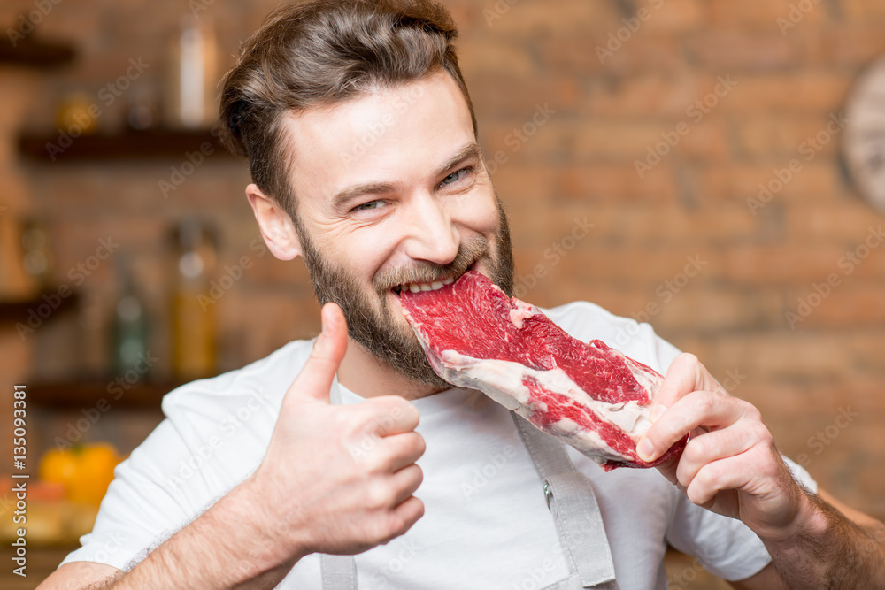 Handsome man biting raw meat on the kitchen