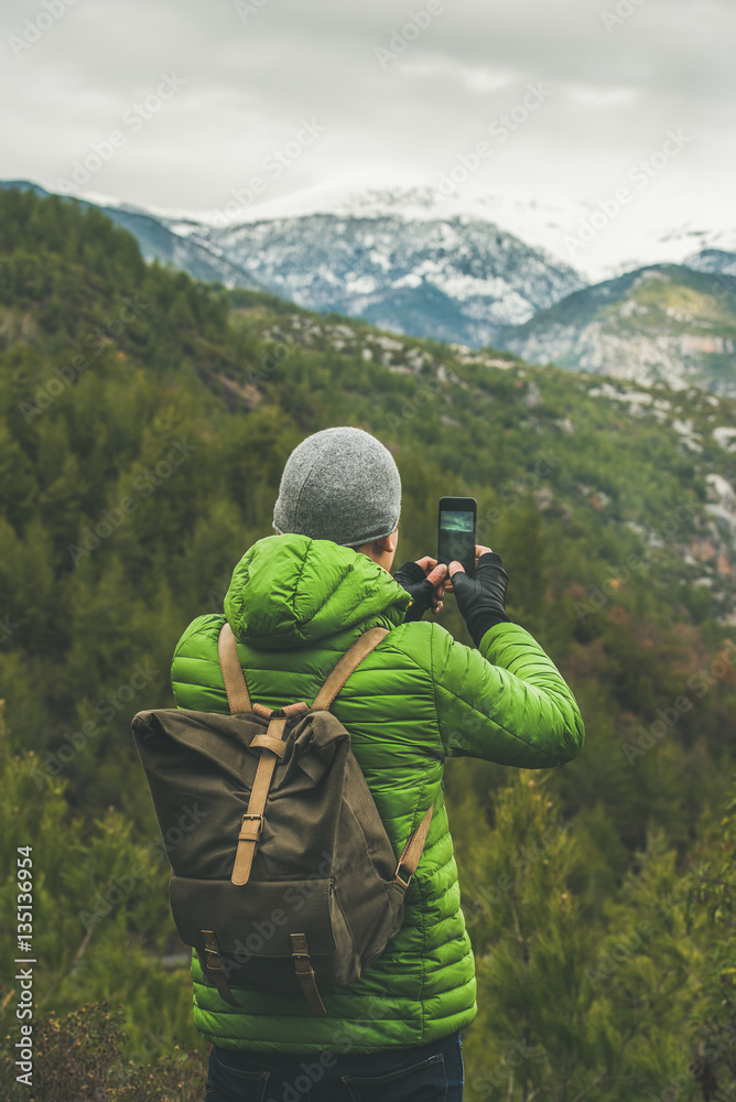 Young man traveller wearing green jacket making photo of slopes and mountains with snowy peaks in Di