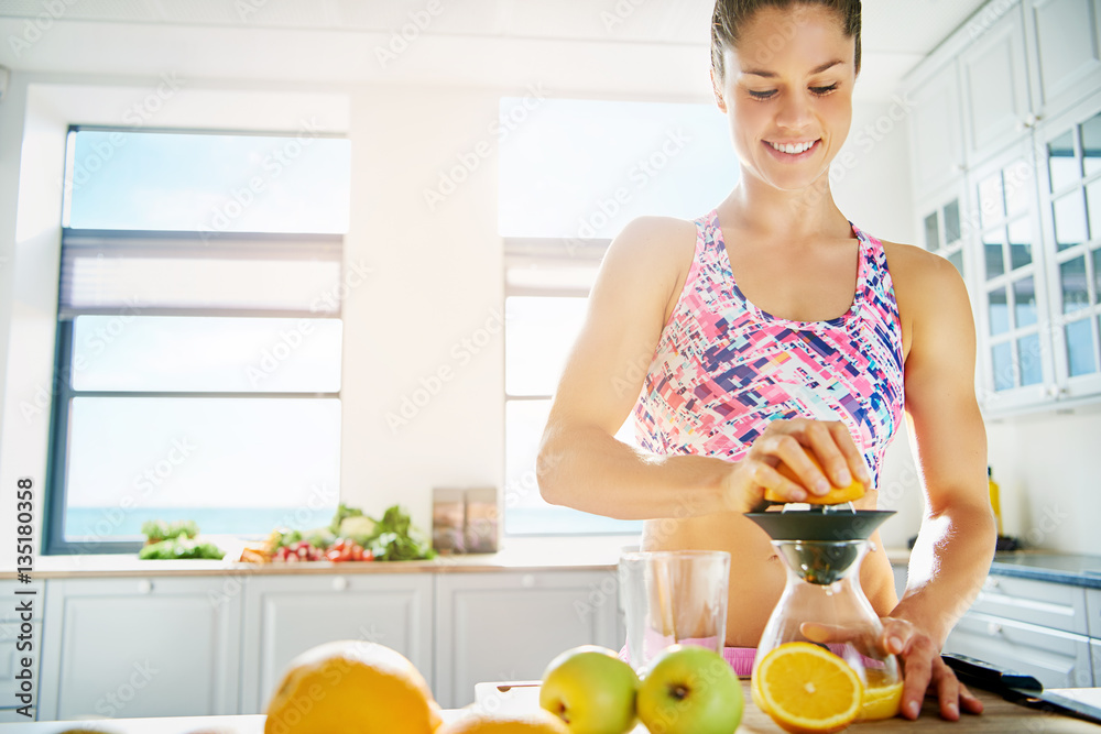 Smiling sportive woman squeezing juice from orange