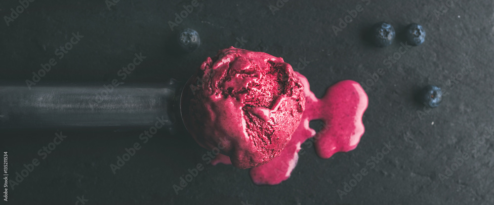 Melting scoop of blueberry ice-cream over black slate stone background, top view, selective focus