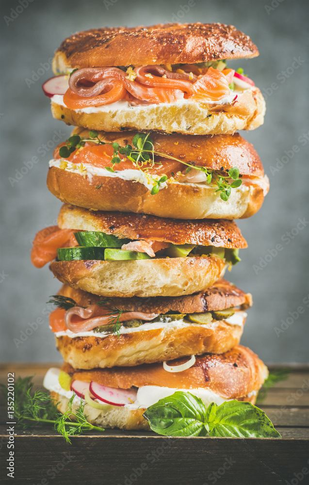 Heap of Bagels with salmon, eggs, vegetables, capers, fresh herbs and cream-cheese, grey concrete ba
