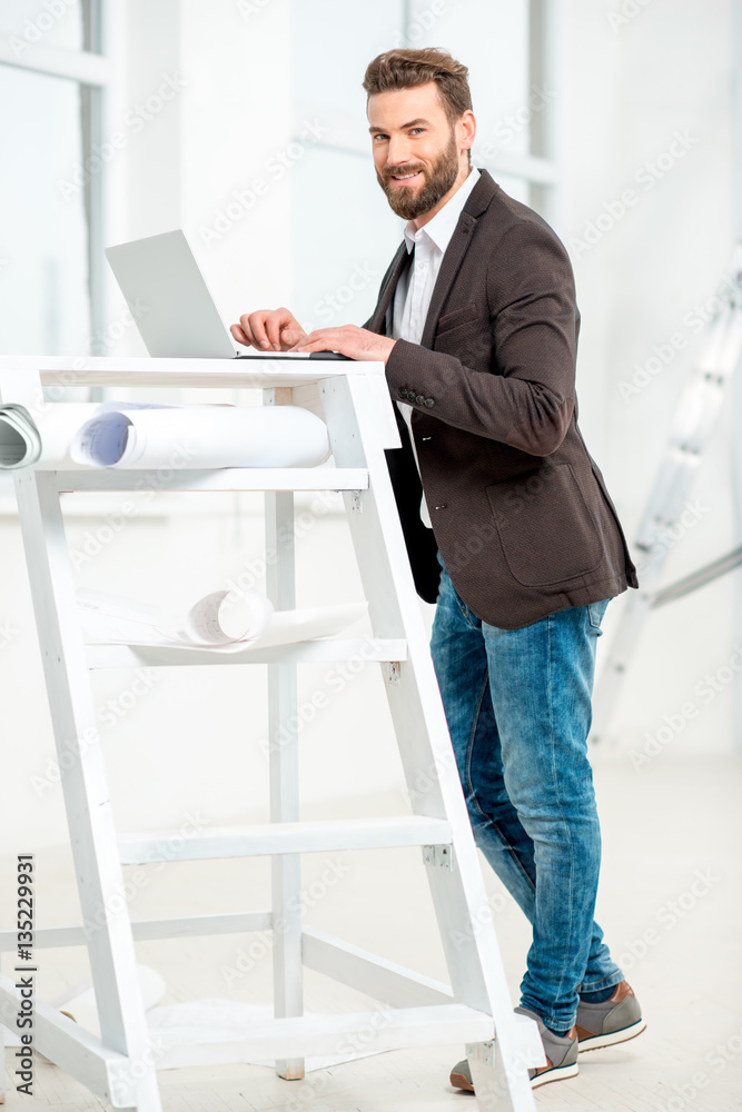 Architect or designer working with laptop on the ladder with paper drawings in the bright room for r