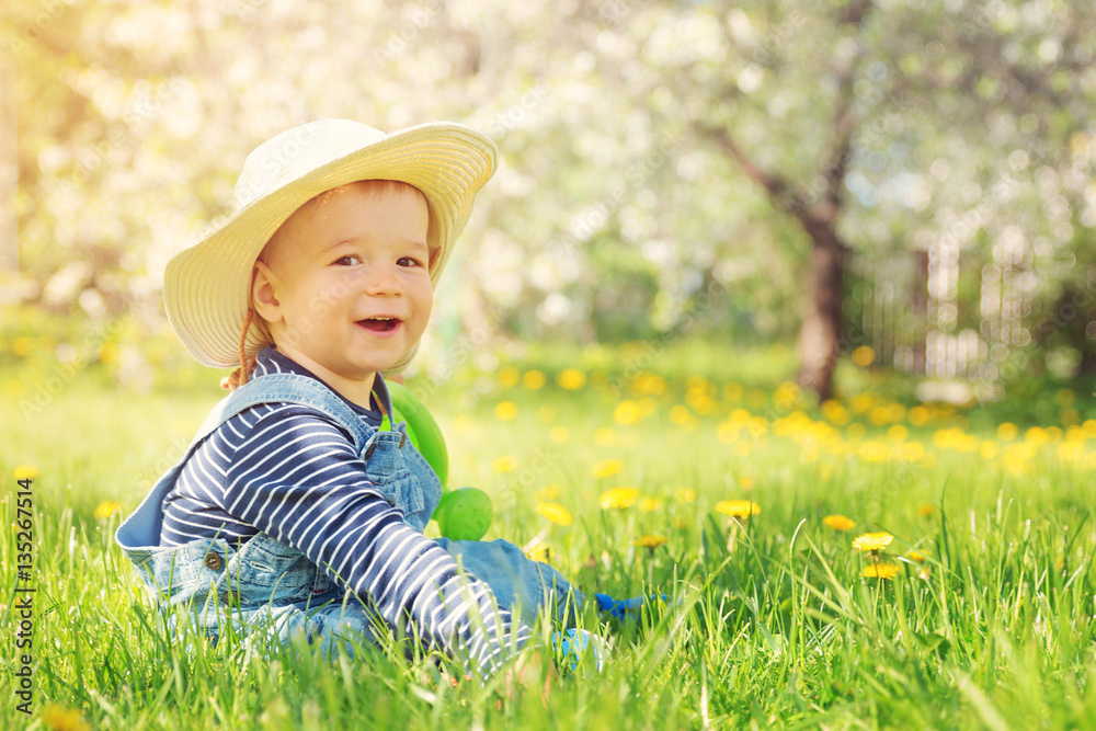 Baby boy sitting on the grass with dandelion flowers in the garden