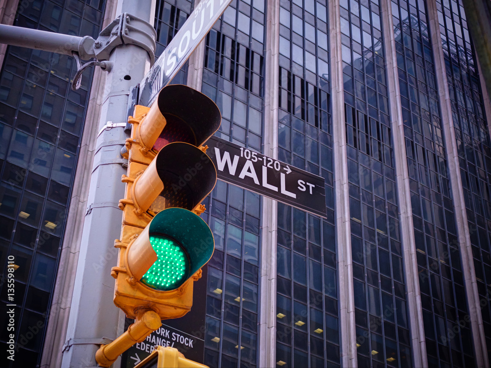 View on wall street yellow traffic light with black and white pointer guide. Green traffic light to 