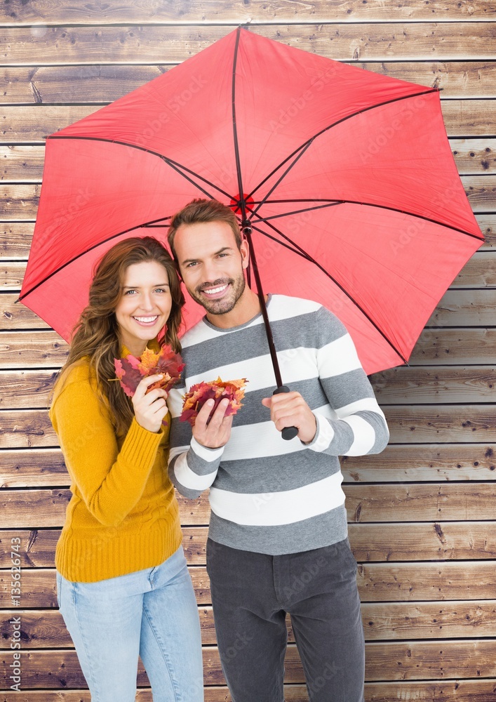 Portrait of happy couple holding umbrella and maple leaves