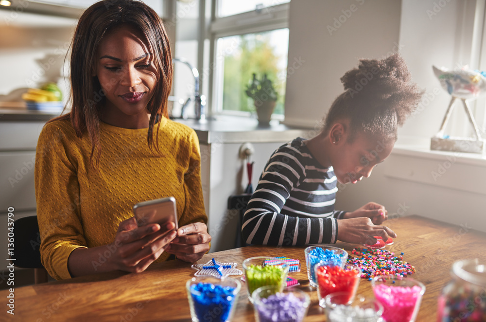 Parent checking phone while girl makes crafts