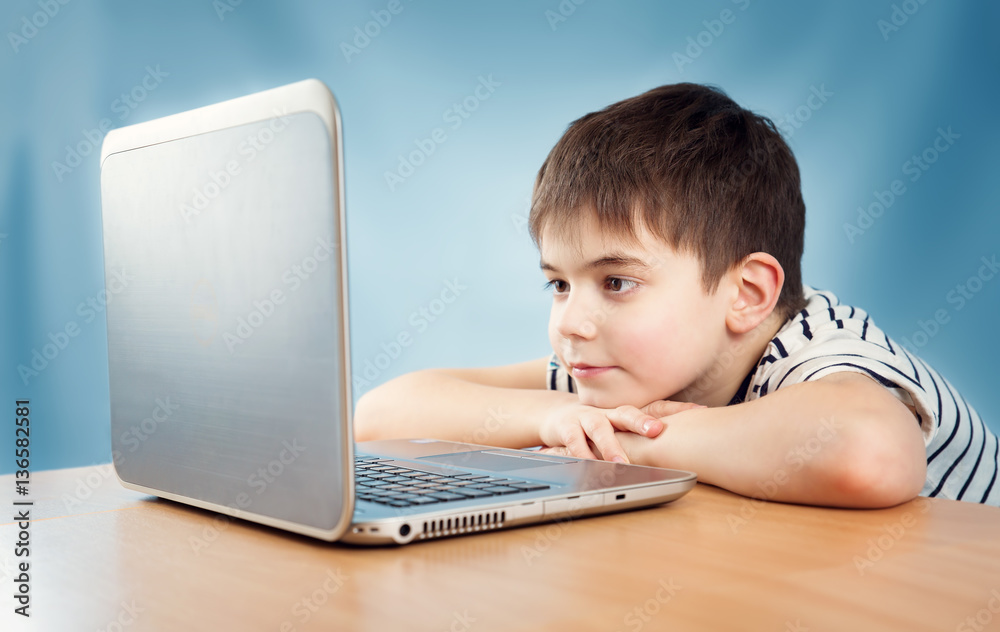 七岁戴眼镜的孩子坐在桌子旁拿着笔记本电脑