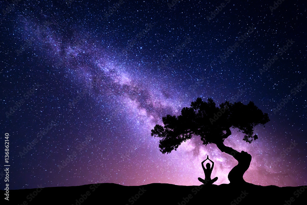 Milky Way with tree and silhouette of a sitting woman practicing yoga. Beautiful landscape with medi