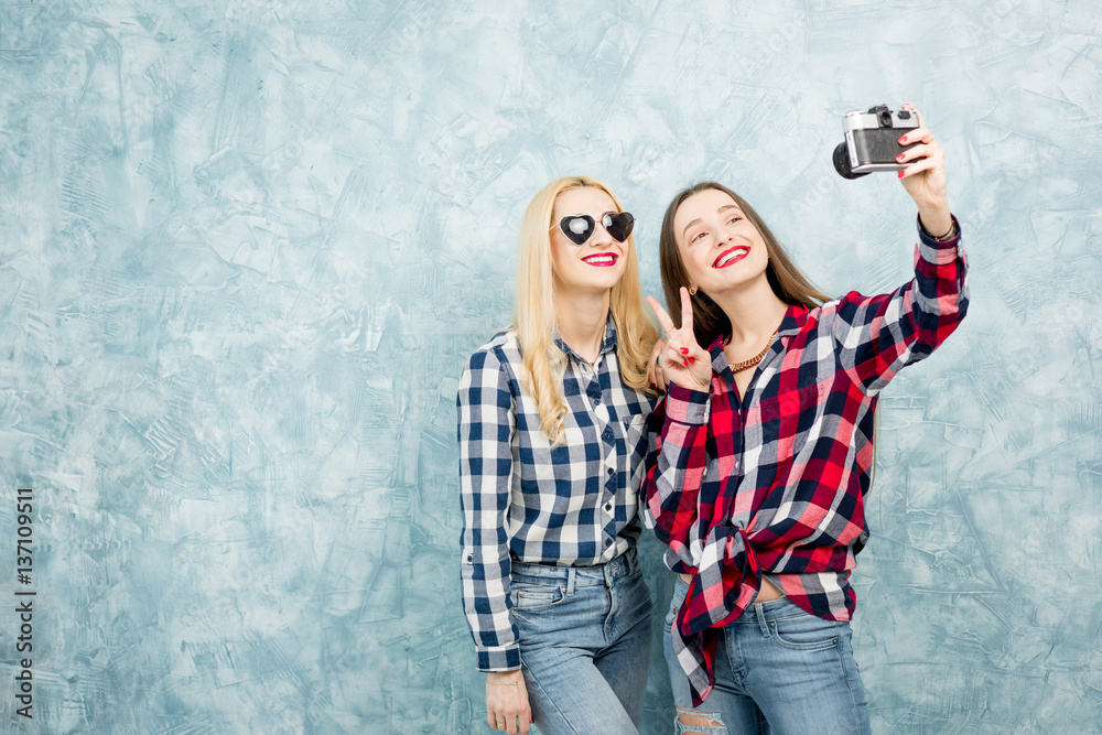 两位穿着格子衬衫和牛仔裤的女性朋友在蓝色油漆上用复古相机拍照
