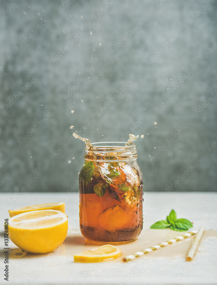 夏季冷冰茶，配新鲜佛手柑、薄荷和柠檬，装在玻璃罐里，在浅色桌子上泼溅。