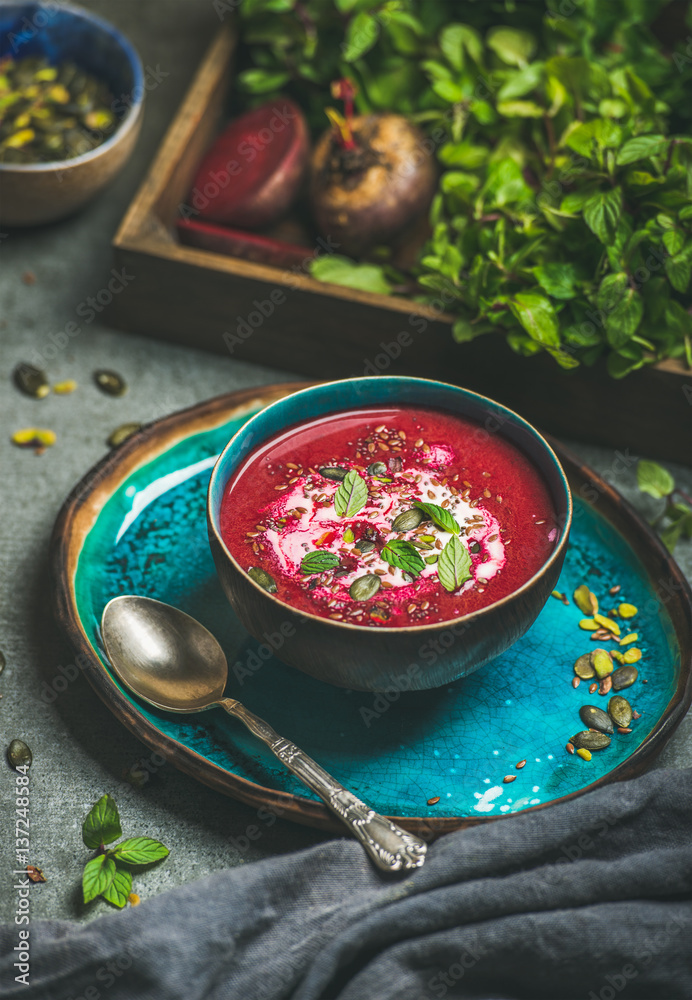 Spring detox beetroot soup with mint, chia, flax and pumpkin seeds in blue ceramic bowl over grey co