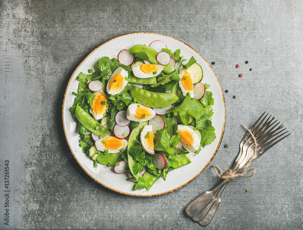 Healthy spring green salad with radish, boiled egg, arugula, green pea and mint in white plate over 