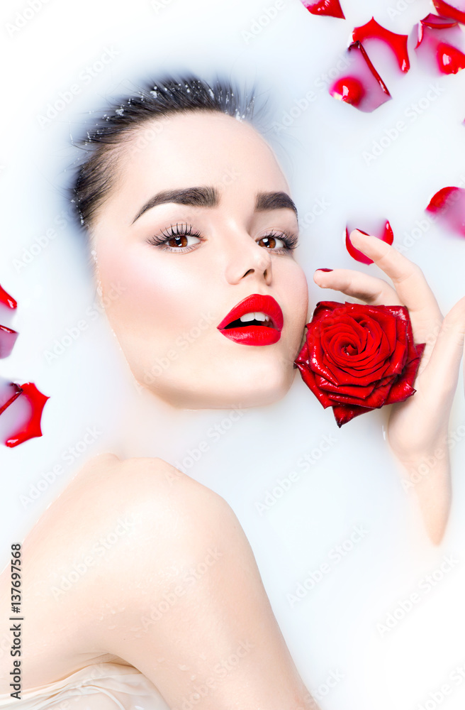 美丽的年轻模特女孩，化着明亮的妆，红玫瑰花在牛奶浴中放松