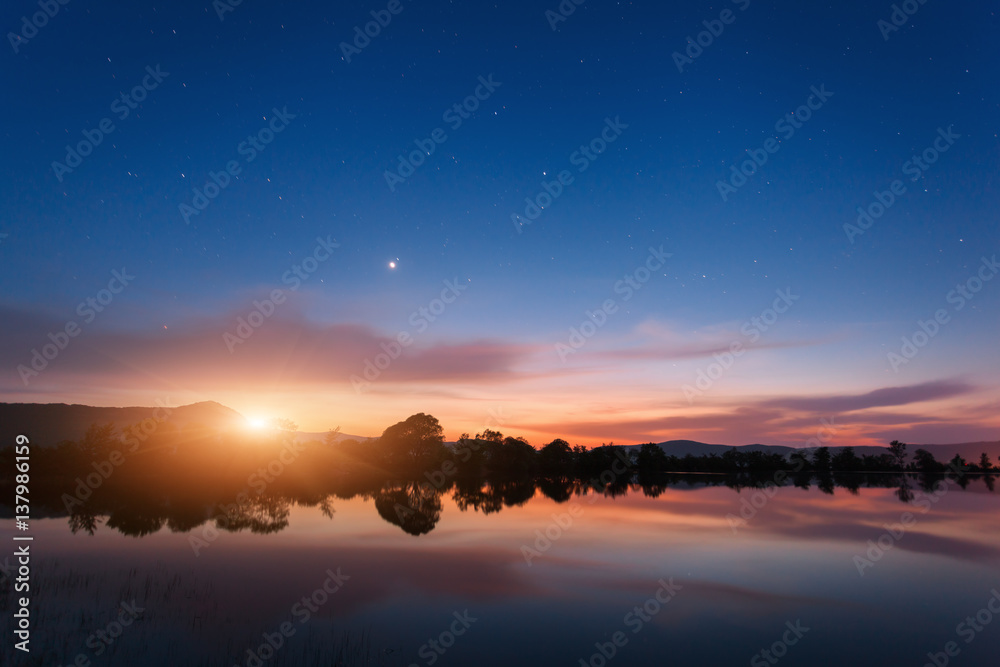 Mountain lake with moonrise at night. Night landscape with river, trees, hills, moon, stars and colo