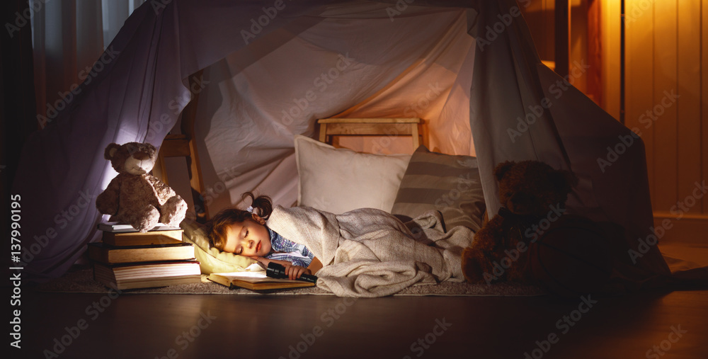 小女孩拿着书和手电筒睡在帐篷里