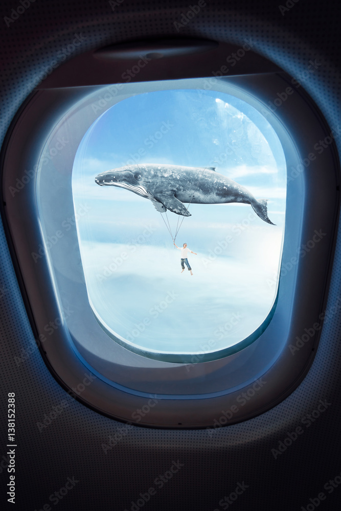Whale floats in the air above the clouds carrying a .young guy ,seen through window of an aircraft ,