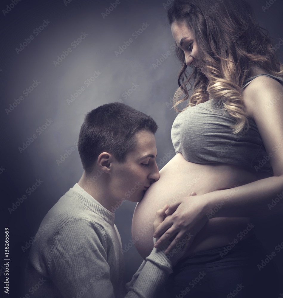 Happy young couple expecting baby. Beautiful pregnant woman and her husband kissing her pregnant bel