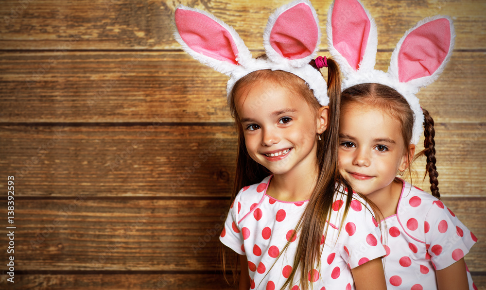 Happy easter! cute twins girls sisters dressed as rabbits  on wooden background